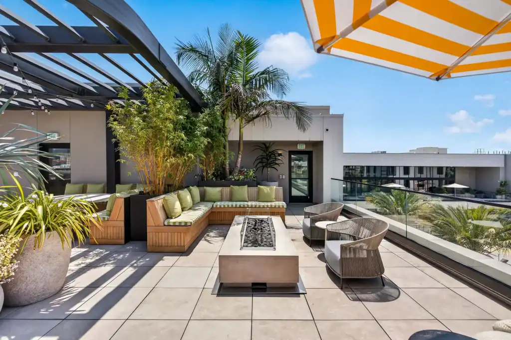 Rooftop terrace with outdoor seating, plants, and a yellow-striped umbrella in a city setting.