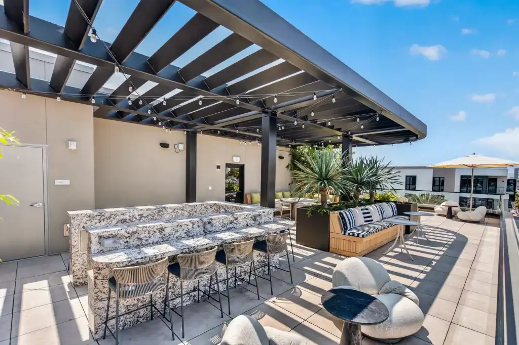 Rooftop patio with modern furniture, pergola, and sunset view in an urban setting.